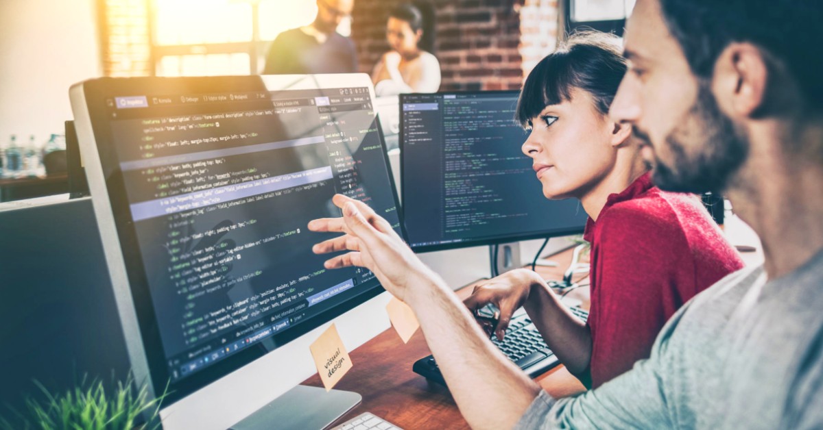 Two people discussing code, at a computer in an office